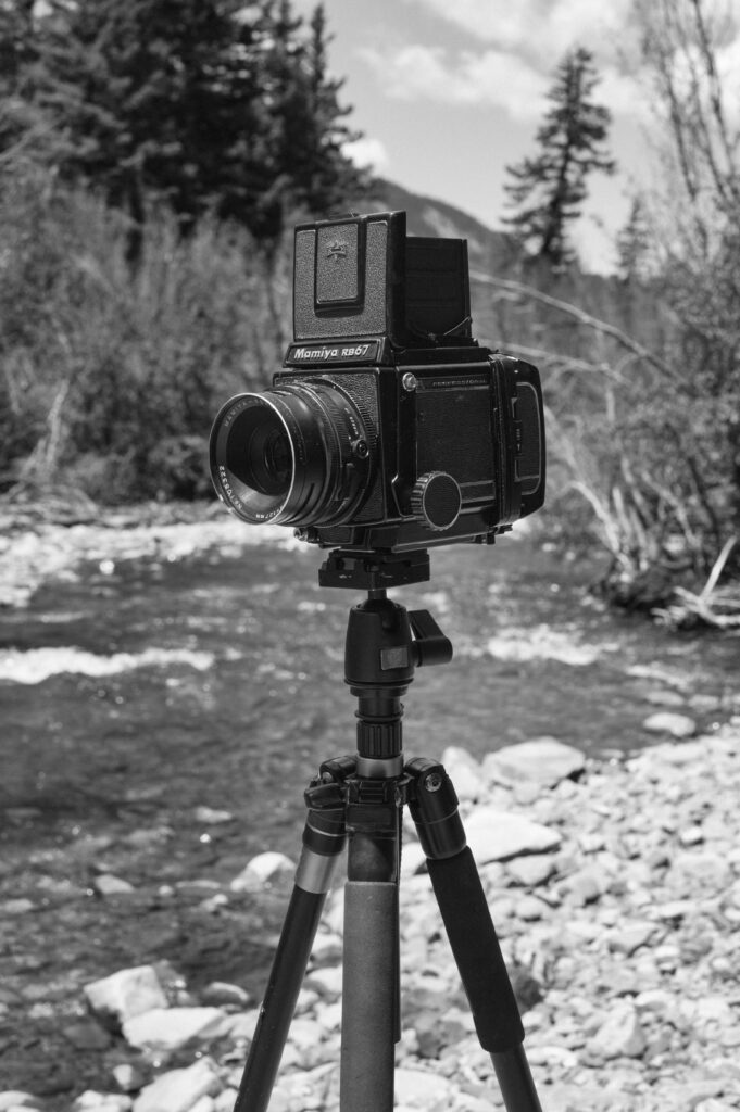 An analog camera Mamiya RZ67 on a stand next to a river in the wilderness